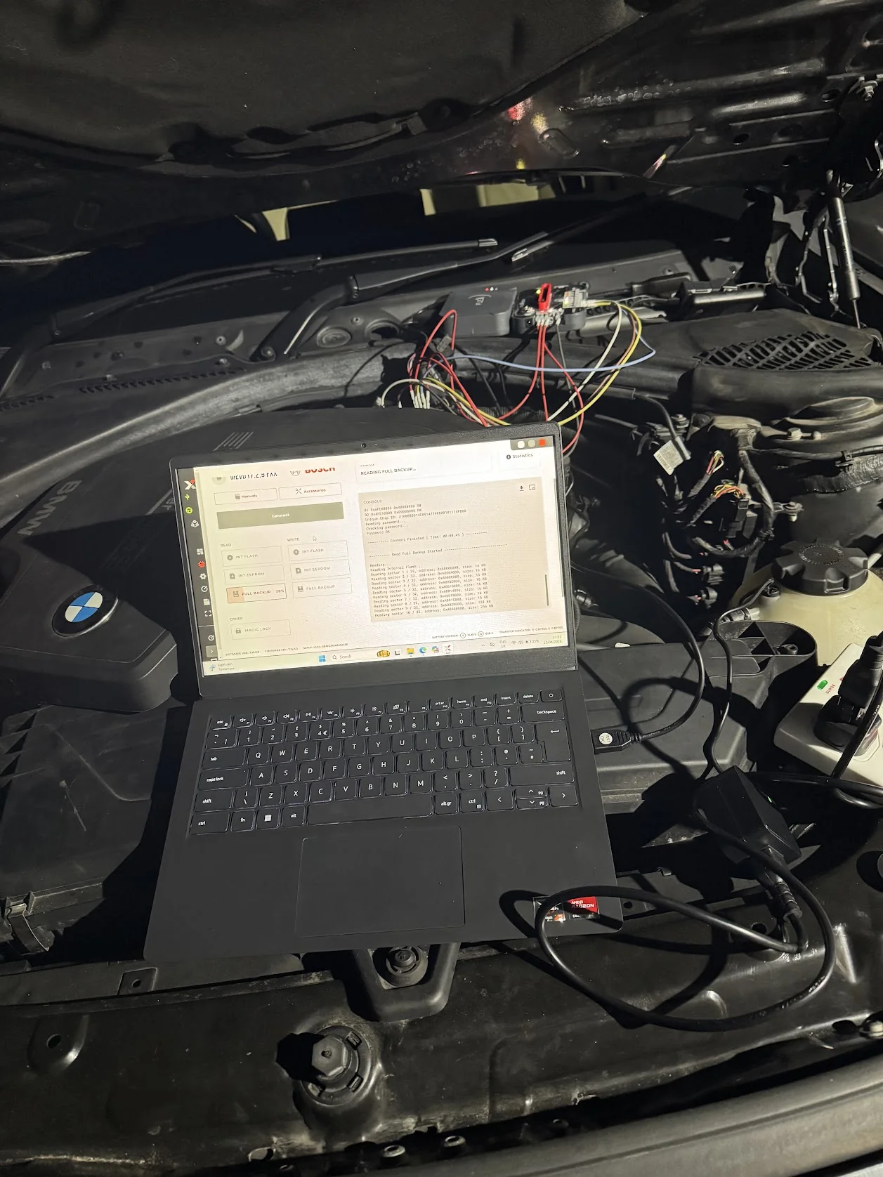 BMW engine bay with laptop running automotive software connected by leads